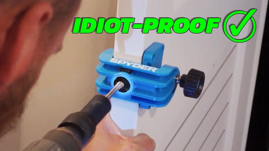 Close-up of the blue Spyder door lock installation jig clamped to a white door with the drill bit perfectly aligned, green ‘IDIOT‑PROOF’ checkmark overlay
